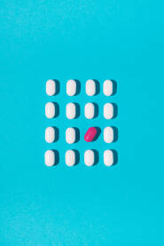 Bijele tablete i jedna ružičasta tableta na plavoj pozadini.