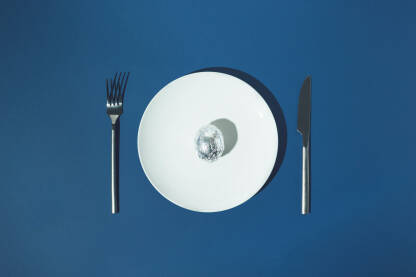 Jaje umotanu u aluminijsku foliju na bijelom tanjuru s viljuškom i nožem sa strane na plavoj pozadini.