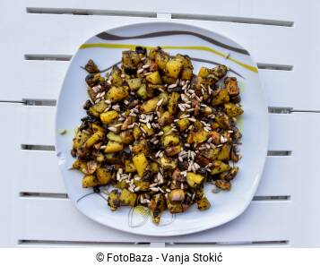 Tanjir sa vegetarijanskim/veganskim obrokom. Pečeni krompir sa gljivama, začinima i sjemenkama suncokreta seviran na bijelom tanjiru i bijelom stolu.