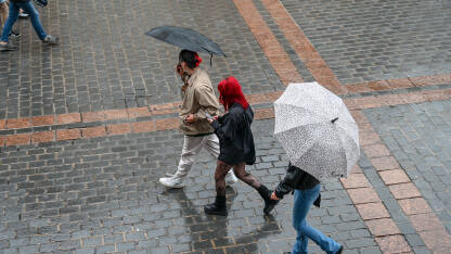 Grupa mladih ljudi šeta gradom sa kišobranima na kiši.