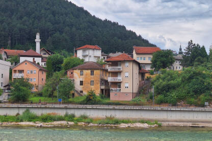 Grad na rijeci Neretvi. Pogled na šetelište obalom rijeke, na srušenu munaru Vardačke džamije, i krov pravoslavne crkve Svetog Vasilija Velikog.