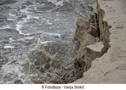 Poplava na moru. Bujica odnosi dio morske obale. Voda razara pješčanu obalu.
