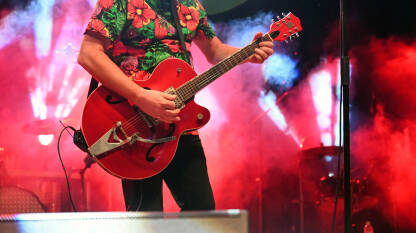 Gitarist svira električnu gitaru na bini tokom koncerta. Muzičar sa gitarom na festivalu.