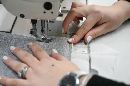 Žena šije tekstil šivaćom mašinom. Radnica radi u fabrici.