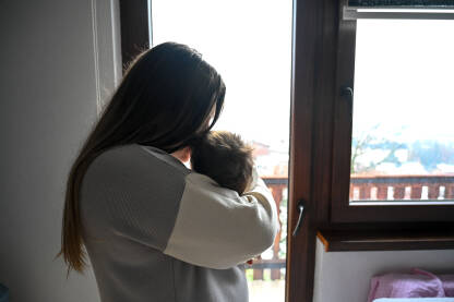 Majka drži bebu blizu prozora. Emocionalna veza između mame i djeteta. Roditelj drži bebu. Žena drži dojenče.