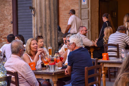 Turisti piju piće u bašti kafića u Italiji. Gosti sjede u bašti lokala. Grupa ljudi pije piće.