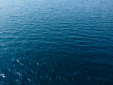 Površina plavog mora, snimak dronom. Odraz sunca na površini vode. Valovi na moru. Duboko plavo more.