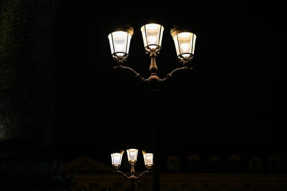 Električna ulična lampa u gradu. Ulična rasvjeta. Upaljena svjetiljka u gradu noću.