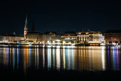 Hamburg, Njemačka. Toranj gradske vijećnice, zgrade i Alster jezera noću. Cityscape. Refleksija svjetla u vodi.