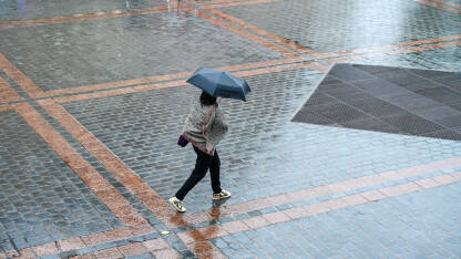 Žena sa kišobranom šeta gradom po kiši.