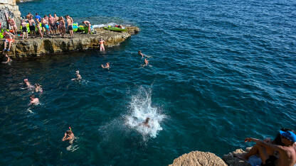 Mladi ljudi se zabavljaju na kamenoj plaži ljeti. Ljudi se sunčaju i kupaju u moru. Ljetna sezona.