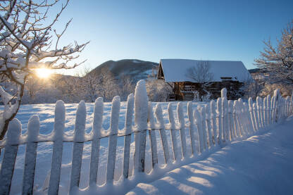 Stara napuštena štala na selu u snijegu obasjana prvim jutarnjim zrakama sunca