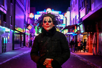 Mladić sa iscrtanom maskom na licu na ulici noću. Muškarac sa maskom Jokera.