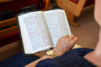 Starija žena se moli u crkvi. Žena drži knjigu tokom molitve. Vjernici se mole.