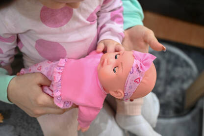 Beba drži lutku. Mama i dijete. Majka drži dijete u naručju. Dijete i igračka.