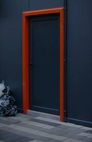 Vrata sive boje kao i zid, narandzasti okvir oko vrata, djubre u kesi ispred vrata