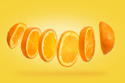 Plutajuće kriške narandže u krupnom planu na žutoj pozadini