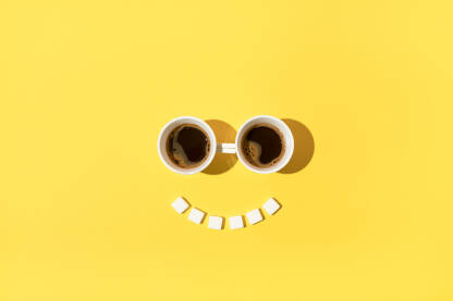 Dvije šalice kave s kockicama šećera na žutoj pozadini.