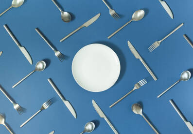 Bijeli tanjur s priborom za jelo na plavoj pozadini.