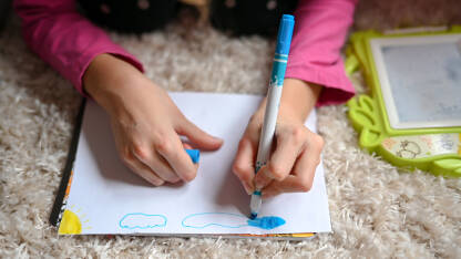 Djevojčica crta kod kuće. Obrazovanje djece. Djevojka piše i crta u svesci za domaći zadatak. Razigrana djeca.