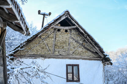 Tradicionalna seoska kuća pokrivena snijegom u selu. Stara rustikalna kuća sa kamenim temeljima i bijelim gipsanim zidovima. Balkanska arhitektura.