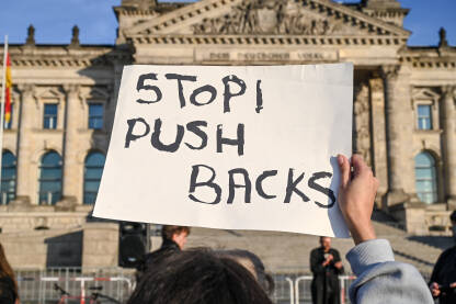 Žena na protestima nosi transparent "Stop Push Backs. Promigrantski protesti. Demonstracije. Grupa ljudi na protestu za ljudska prava i slobode.