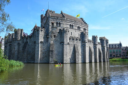 Gent, Belgija: Dvorac uz riječni kanal u središtu grada. Turisti na brodu istražuju grad. Utvrđene kule i zidovi na srednjovjekovnom utvrđenju. Dvorac Gravensteen.