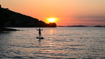 Djevojka  na dasci na moru na zalasku sunca. Žena uživa na Paddle-boardu tokom ljeta.