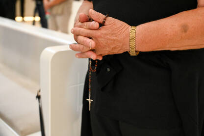 Žena drži krunicu u rukama tokom molitve u crkvi. Misa u katedrali. Žena se moli.