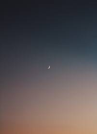 Mlad mjeseca na cistom nebu uz zalazak sunca.