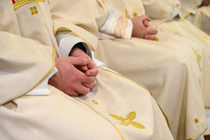 Katolički svećenici u liturgijskim odorama se mole prekrštenih ruku.  Božićna ponoćna misa u crkvi. Biskupi