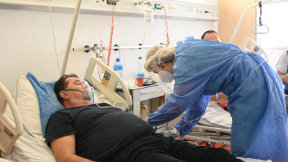 Čovjek na respiratoru u bolnici. Medicinska sestra s pacijentom zaraženim koronavirusom leži u klinici. Pacijent sa COVID-om leži u bolničkom krevetu na respiratoru.