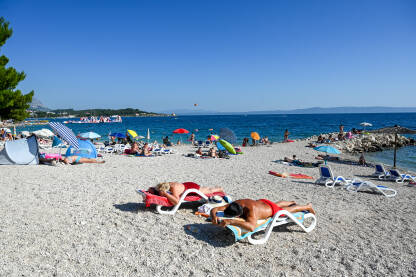 Makarska, Hrvatska: Turisti na plaži i u moru. Ljetni godišnji odmori. Obala Jadraskog mora ljeti. Turistička sezona. Ljudi se sunčaju i kupaju.