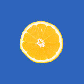 Svježa žuta narandža presječena na pola na svijetloj jarkoplavoj podlozi.