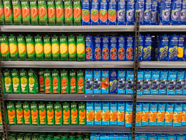 Raznovrsna pakovanja voćnih sokova u supermarketu. Polica popunjena asortimanom voćnih sokova različitih okusa, uključujući narandžu, limun, jabuku i bobičasto voće.