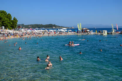 Turisti na moru. Ljudi se kupaju i sunčaju u Jadranskom moru. Ljetni odmor. Grupa turista na plaži tokom toplog ljetnog dana. Makarska, Hrvatska.