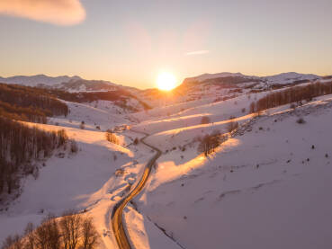 Zalazak sunca u planinama zimi, snimak dronom. Snijeg na brdima i dolinama u decembru. Miran zalazak sunca u prirodi. Planine Bjelašnica i Visočica, Bosna i Hercegovina.