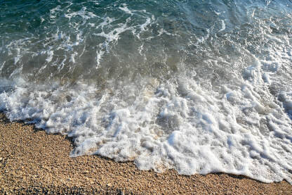 Morski valovi na plaži sa sitnim zlatnim pijeskom. Talasi na obali mora tokom zalaska sunca ljeti.