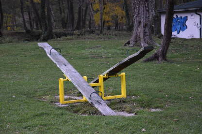 Klackalica za djecu napravljena od drveta i metala u prirodnom okruženju sa malim objektom u pozadini.