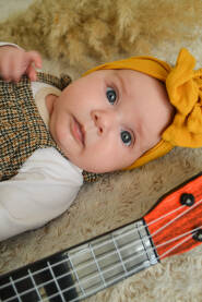 Slatka beba pored gitare, sa žutom mašnom na glavi, pozira za fotografiju.