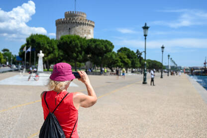 Žena fotografiše mobilnim telefonom u gradu. Turisti slikaju ulice i građevine. Šetalište u Solunu, Grčka.