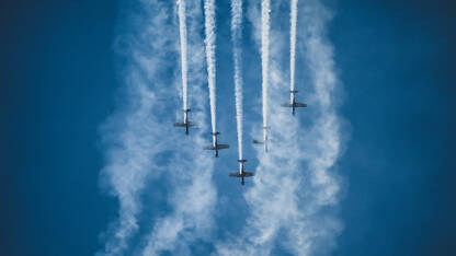 Avioni na plavom nebu tokom aeromitinga. Pet aviona u formaciji. Avioni u letu sa dimnim tragovima.