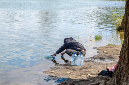 Migrant sipa vodu u flaše iz rijeke. Muškarac sa plastičnim bocama sipa vodu.