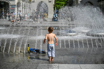 Dječak se osvježava na fontani. Dijete se osvježava pod vodom tokomm vrelog ljetnog dana. Toplotni talas u gradu. Dječak je poprskan vodom.