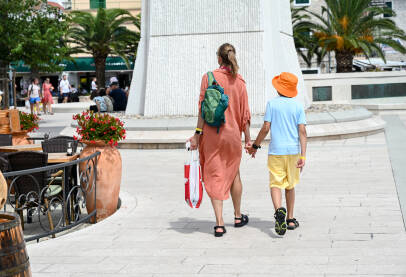 Majka sa sinom šeta ulicom. Majka drži dijete za ruku.