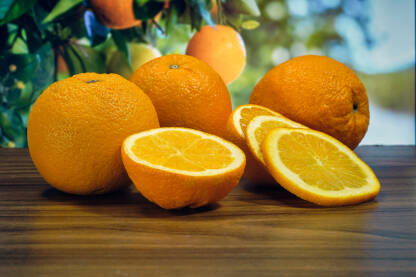 Narandže i kriške na stolu u pozadini plodovi na granama
