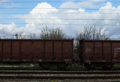 Dva braon vagona na pruzi, beli oblaci u pozadini, kamenje, pruga