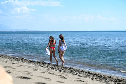 Dvije djevojke šetaju pješčanom plažom uz more. Turisti na odmoru. Žene u kupaćim kostimima šetaju uz more.