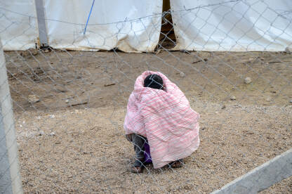 Migrant se smrzava u kampu ograđenom žicom. Čovjek umotan u deku. Izbjeglice na Balkanskoj ruti tokom zime. Kamp Lipa, Bihać, BiH.