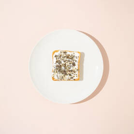 Kriška tost hruha namazana krem sirom i posuta zlatnim perlama na bijelom tanjuru.